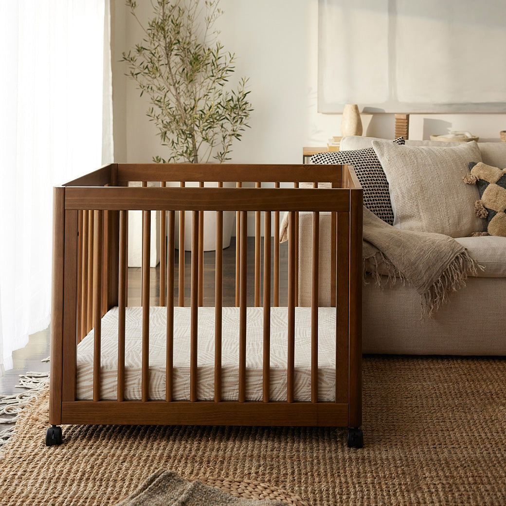 Babyletto's Yuzu 8-In-1 Convertible Crib next to a couch  in -- Color_Natural Walnut