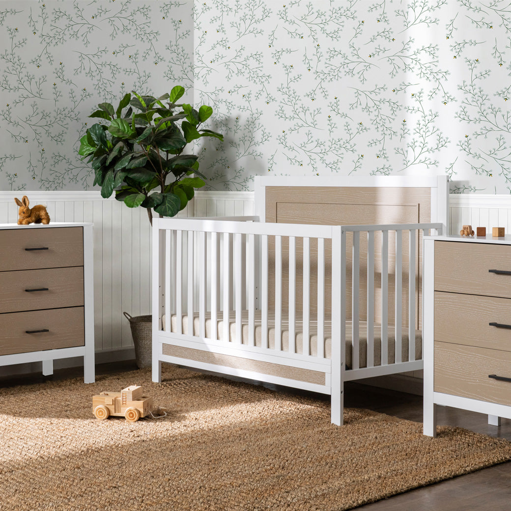 Carter's by DaVinci Radley 4-in-1 Convertible Crib next to two dressers and a plant  in -- Color_White/Coastwood
