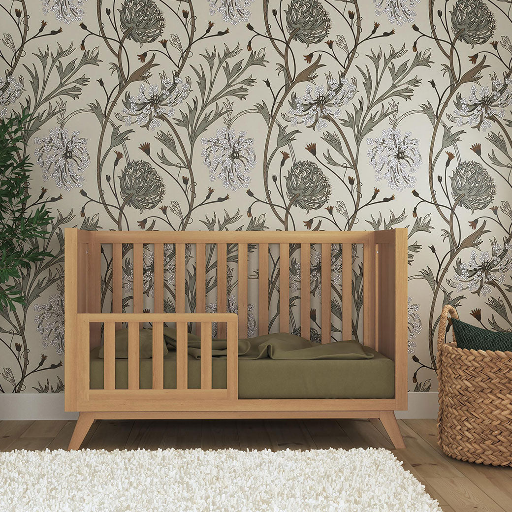 DaVinci Otto 3-in-1 Convertible Crib as a toddler crib next to a plant and basket  in -- Color_Honey _ Wood
