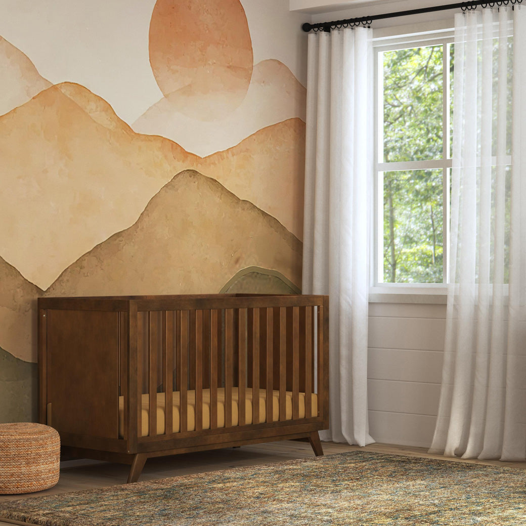 DaVinci Otto 3-in-1 Convertible Crib next to a window in -- Color_Walnut _ Wood