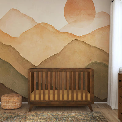 Front view of DaVinci Otto 3-in-1 Convertible Crib in a sunset and mountains room  in -- Color_Walnut _ Wood
