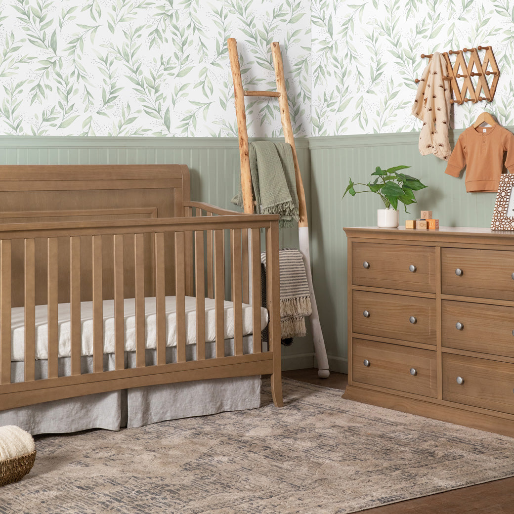 DaVinci Anders 4-in-1 Convertible Crib next to a dresser in -- Color_Hazelnut