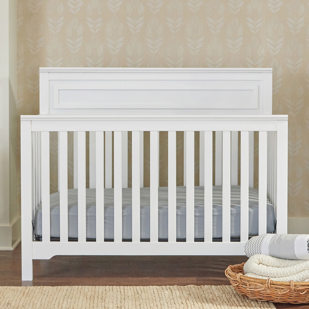 Front view of DaVinci Autumn 4-in-1 Convertible Crib next to a basket in -- Color_White