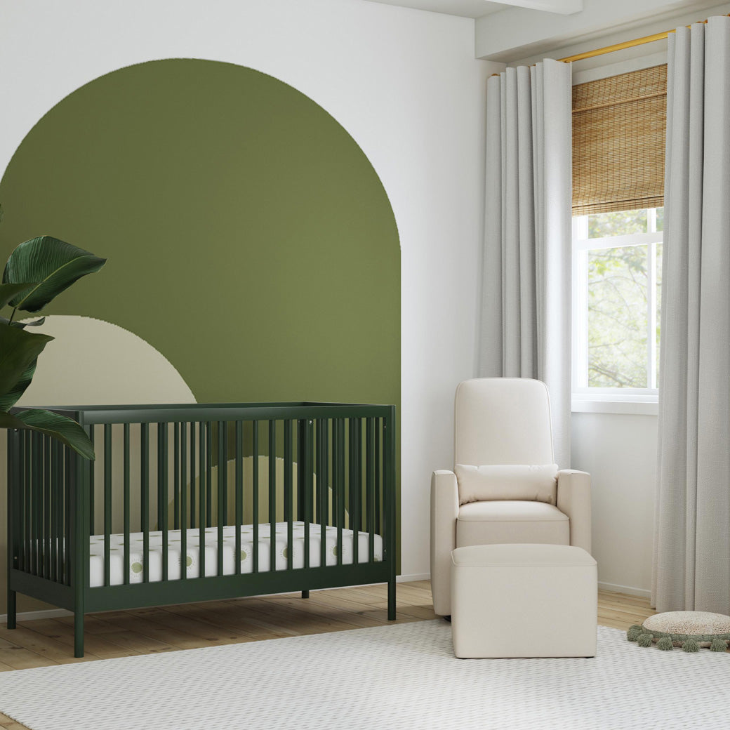 DaVinci Birdie 3-in-1 Convertible Crib next to a recliner and ottoman  in -- Color_Forest Green