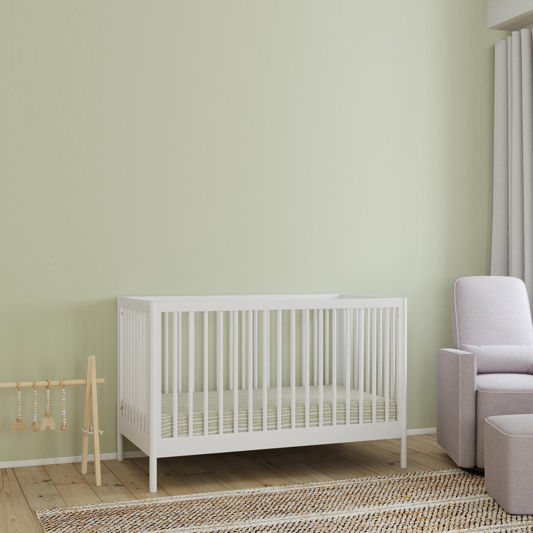 DaVinci Birdie 3-in-1 Convertible Crib  next to a play toy bar and recliner in -- Color_White
