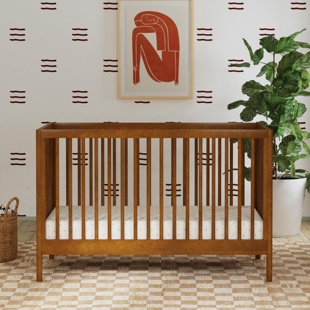 Front view of DaVinci Birdie 3-in-1 Convertible Crib next to a plant in -- Color_Walnut