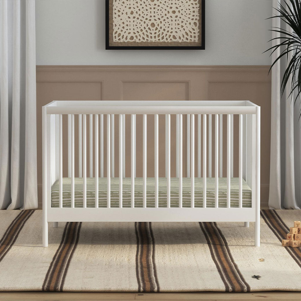 Front view of DaVinci Birdie 3-in-1 Convertible Crib next to a plant in -- Color_White