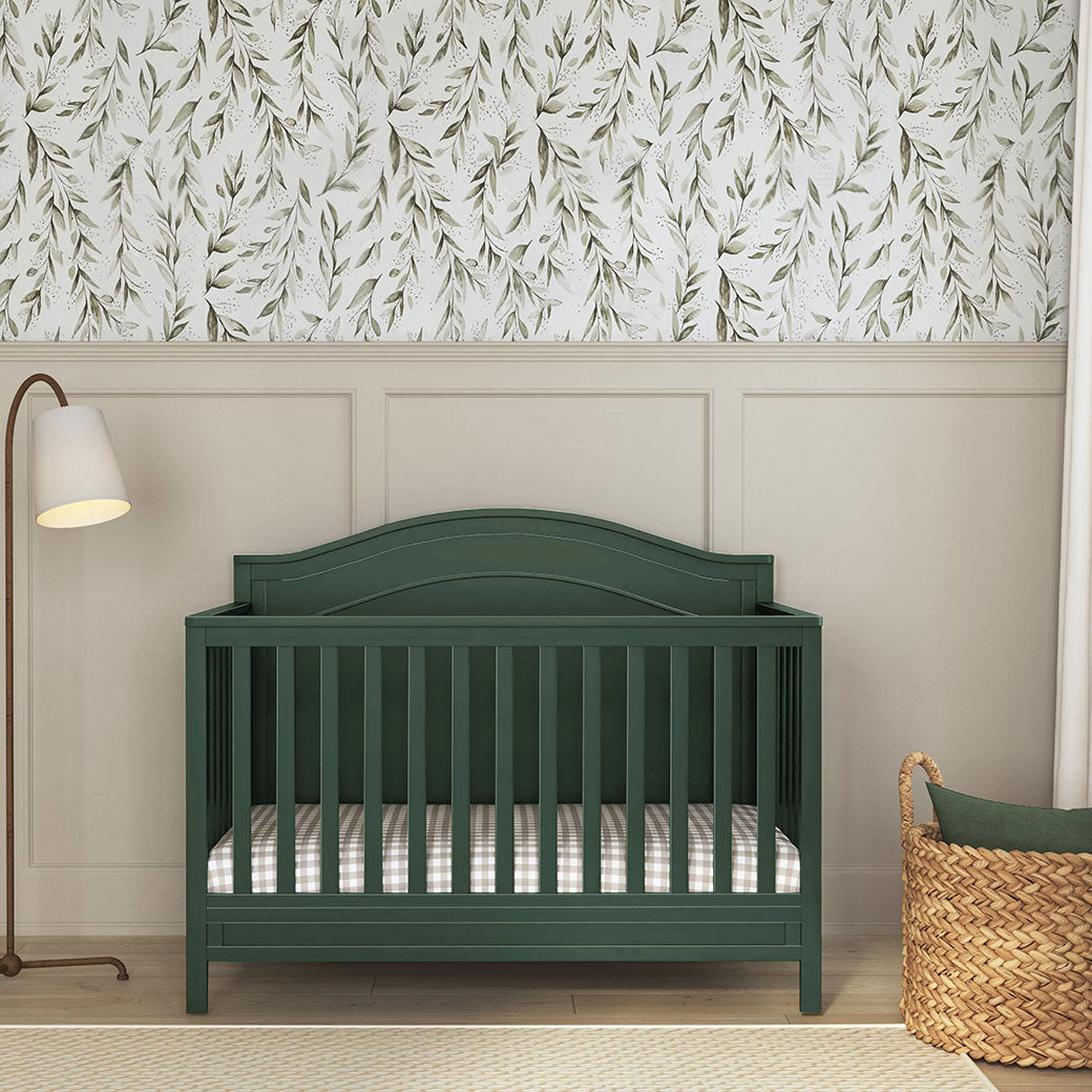Front view of Front view of The DaVinci Charlie 4-in-1 Convertible Crib next to a lamp and basket in -- Color_Forest Green