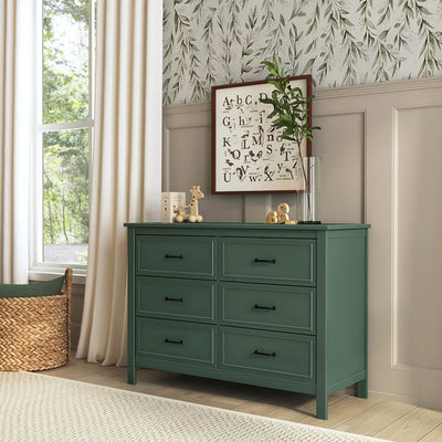 The DaVinci Charlie 6-Drawer Dresser next to a window and basket  in -- Color_Forest Green