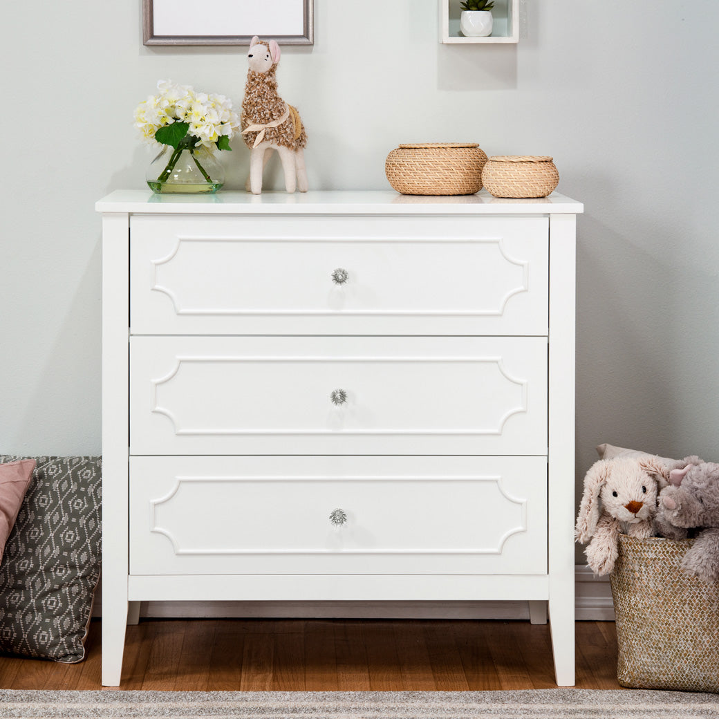 Front view of DaVinci Chloe Regency 3-Drawer Dresser next to pillows and a basket  in -- Color_White 