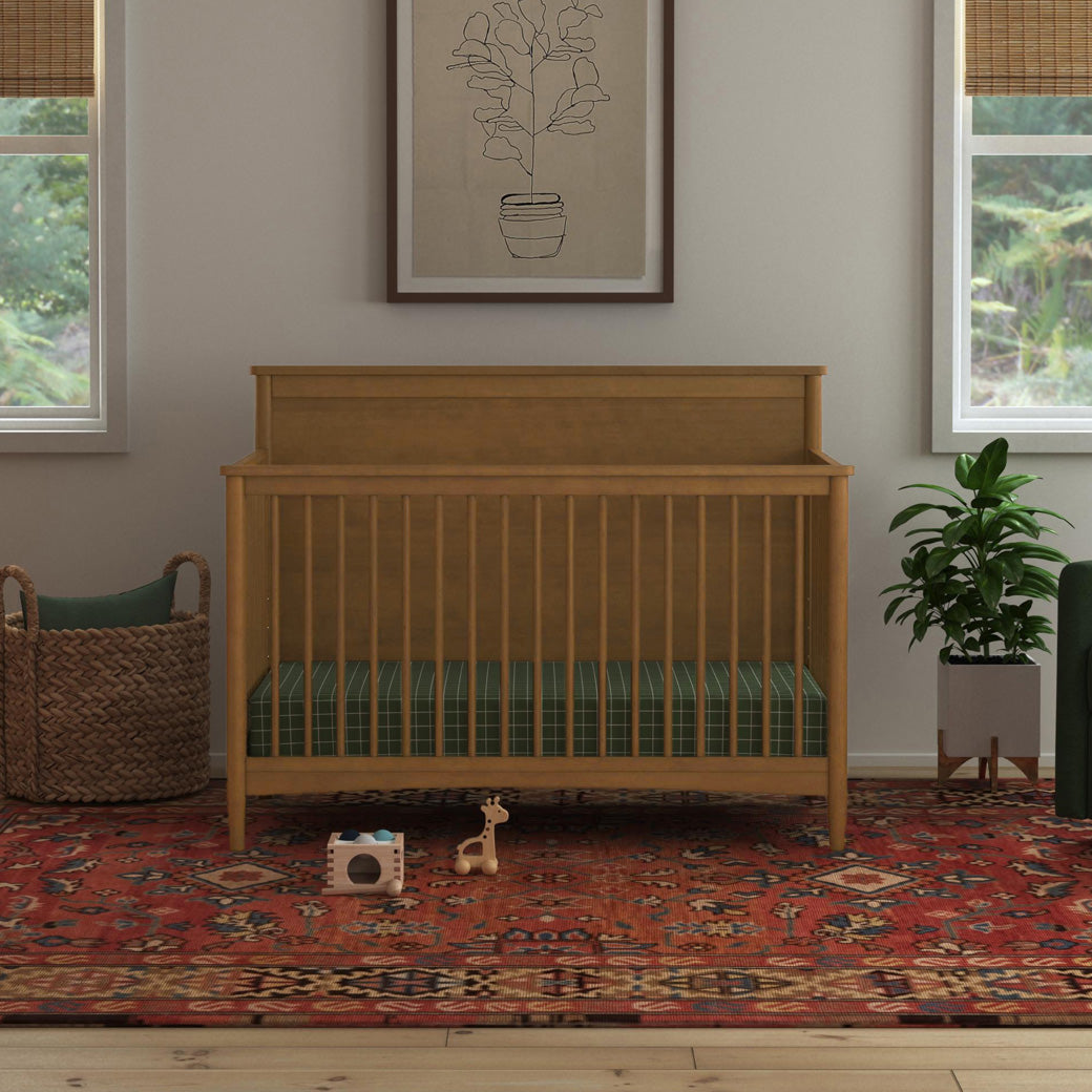Front view of DaVinci Frem 4-in-1 Convertible Crib next to basket and plant  in -- Color_Walnut
