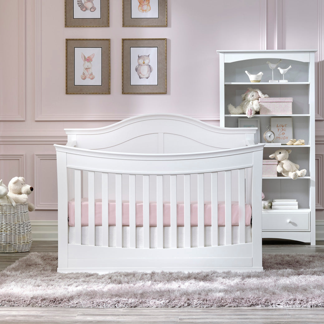 Front view of DaVinci Meadow 4-in-1 Convertible Crib next to a basket and bookshelf in -- Color_White