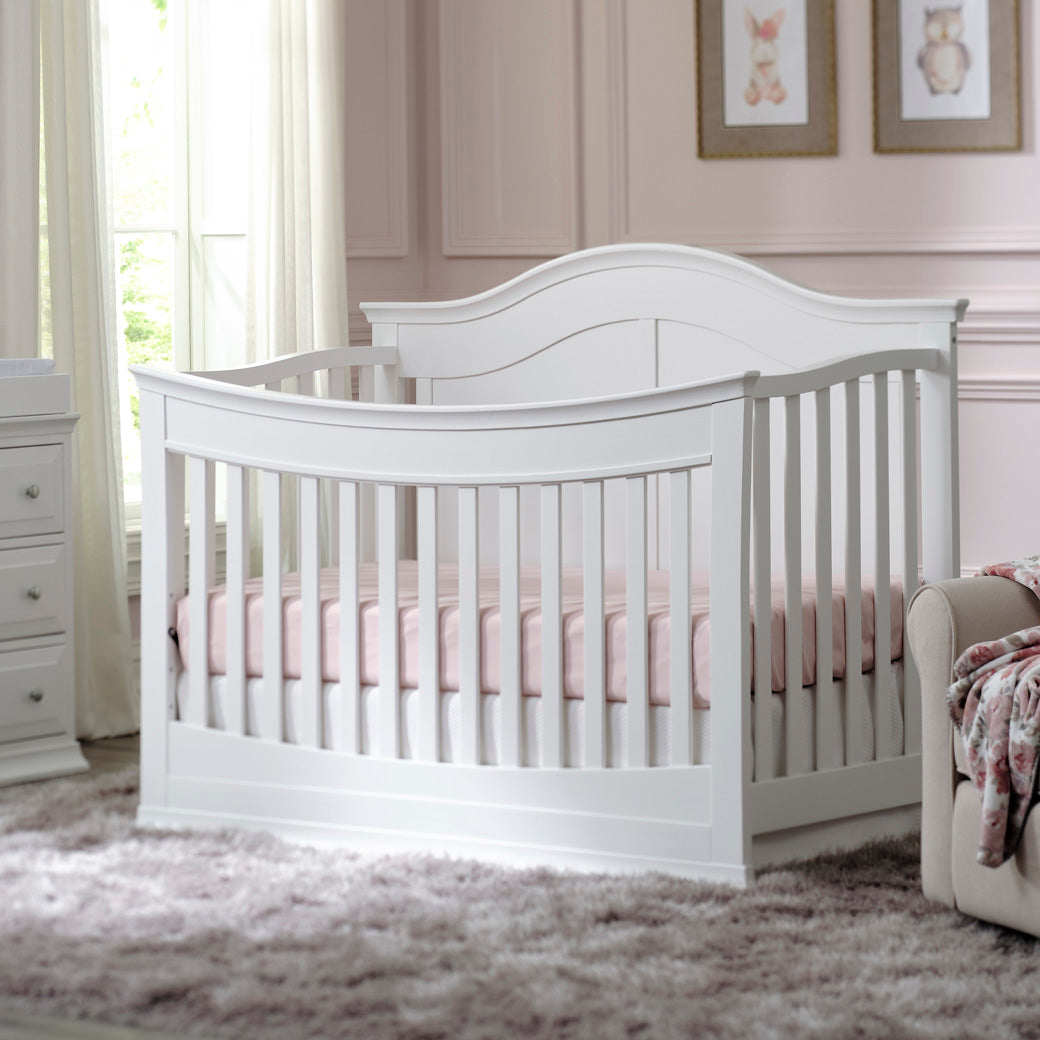 DaVinci Meadow 4-in-1 Convertible Crib next to a dresser and recliner  in -- Color_White