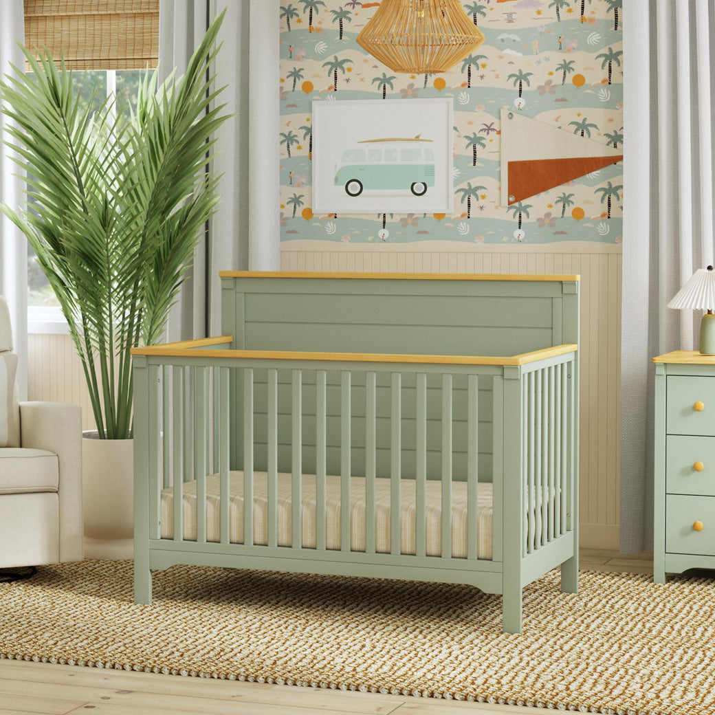 DaVinci Shea 4-in-1 Convertible Crib next to a plant and dresser  in -- Color_Light Sage/Honey