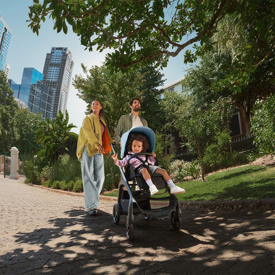 Mom and dad with a child in a park pushing a stroller with the Bugaboo Dragonfly Sun Canopy in -- Color_Skyline Blue