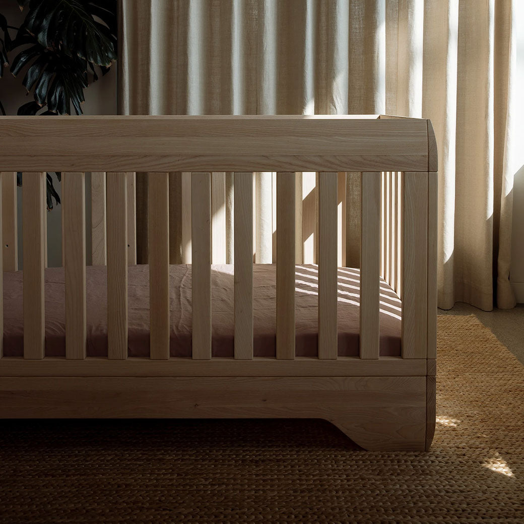 Right side view of Kalon Echo Crib in front of a curtain  in -- Color_Ash