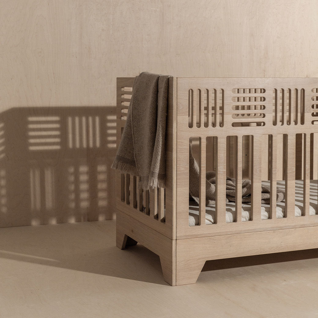 Slight side view of the Kalon Io Crib with a blanket inside  -- Lifestyle