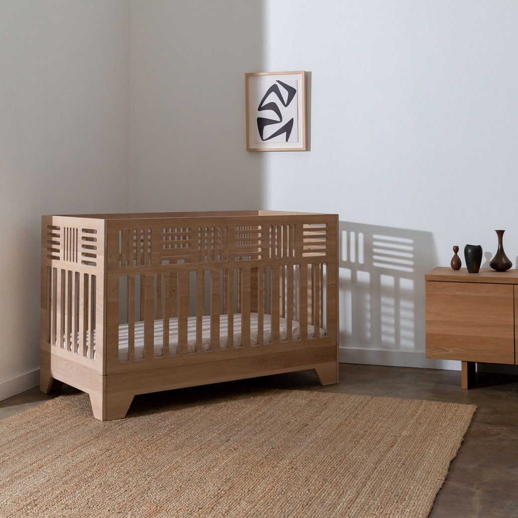 The Kalon Io Crib in the corner of a room next to a picture and a dresser  -- Lifestyle