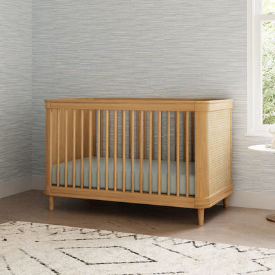 The Namesake Marin 3-in-1 Convertible Crib next to a window in -- Color_Honey/Honey Cane