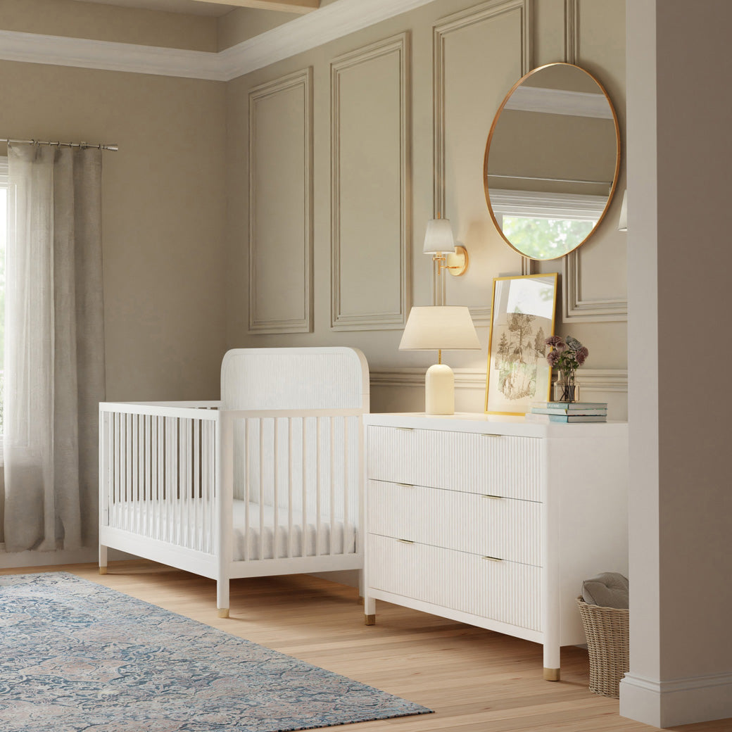 Side view of Namesake Brimsley 4-in-1 Convertible Crib next to a dresser in -- Color_Warm White