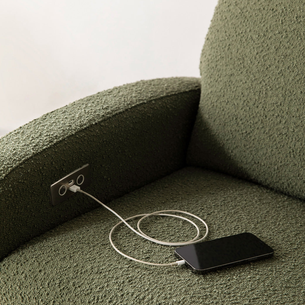 The Babyletto Nami Glider Recliner with a phone charging on the USB port  in -- Color_Olive Boucle with Light Wood Base