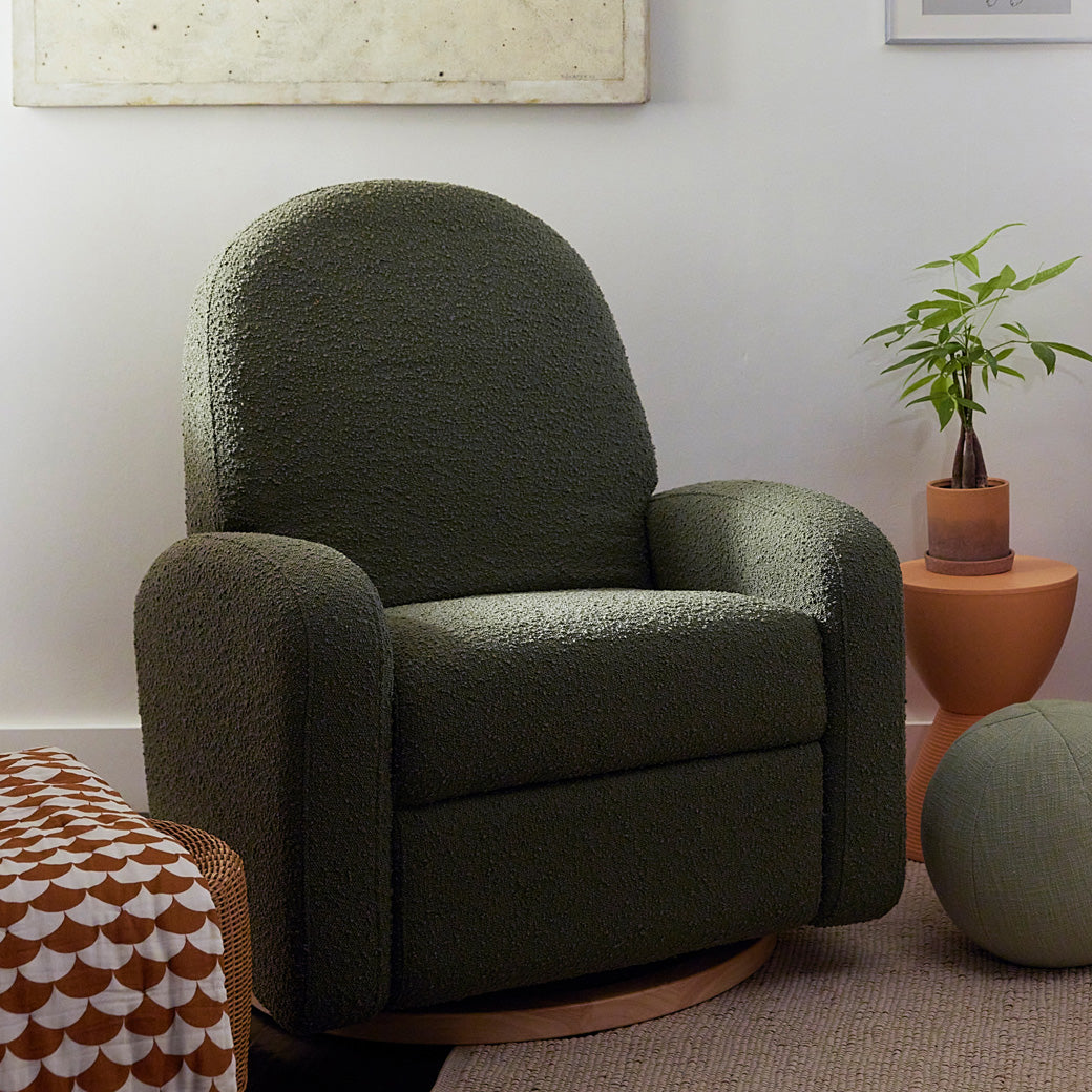 The Babyletto Nami Glider Recliner next to a table with a plant on it in -- Color_Olive Boucle with Light Wood Base