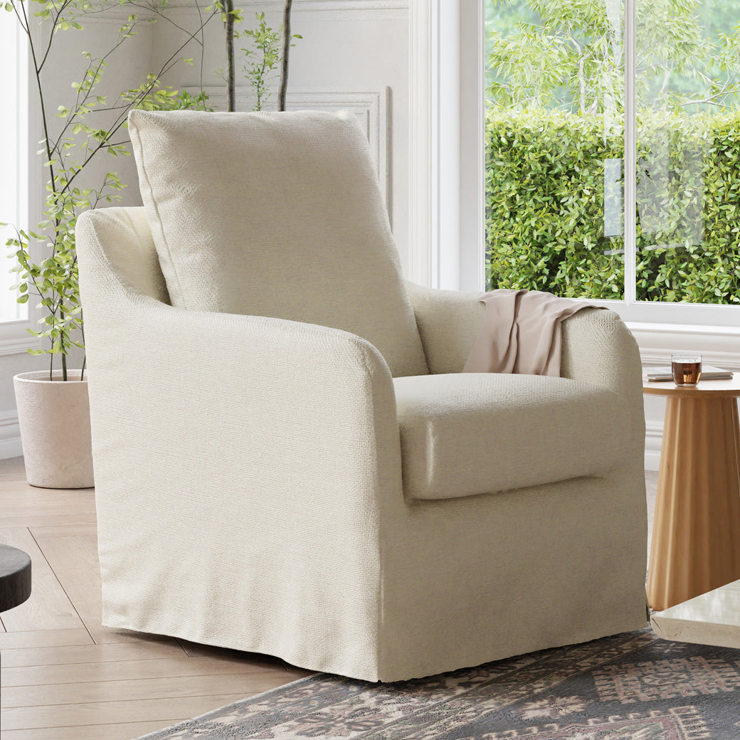Namesake Reese Slipcover Swivel Glider next to coffee table and window -- Color_Ivory Eco-Linen