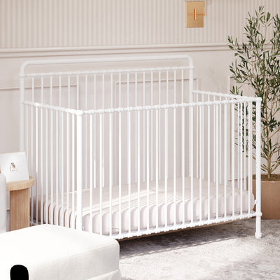 Namesake's Winston 4 in 1 Convertible Crib next to a plant and ottoman in -- Color_Washed White