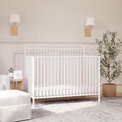 Namesake's Winston 4 in 1 Convertible Crib under some lamps and next to a lamp and ottoman  in -- Color_Washed White