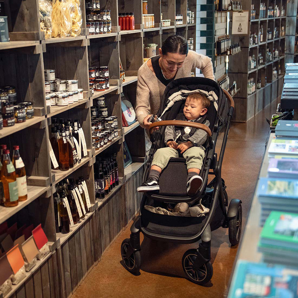 Mom in the store with her baby sitting in the Nuna DEMI Next Stroller in -- Color_Caviar