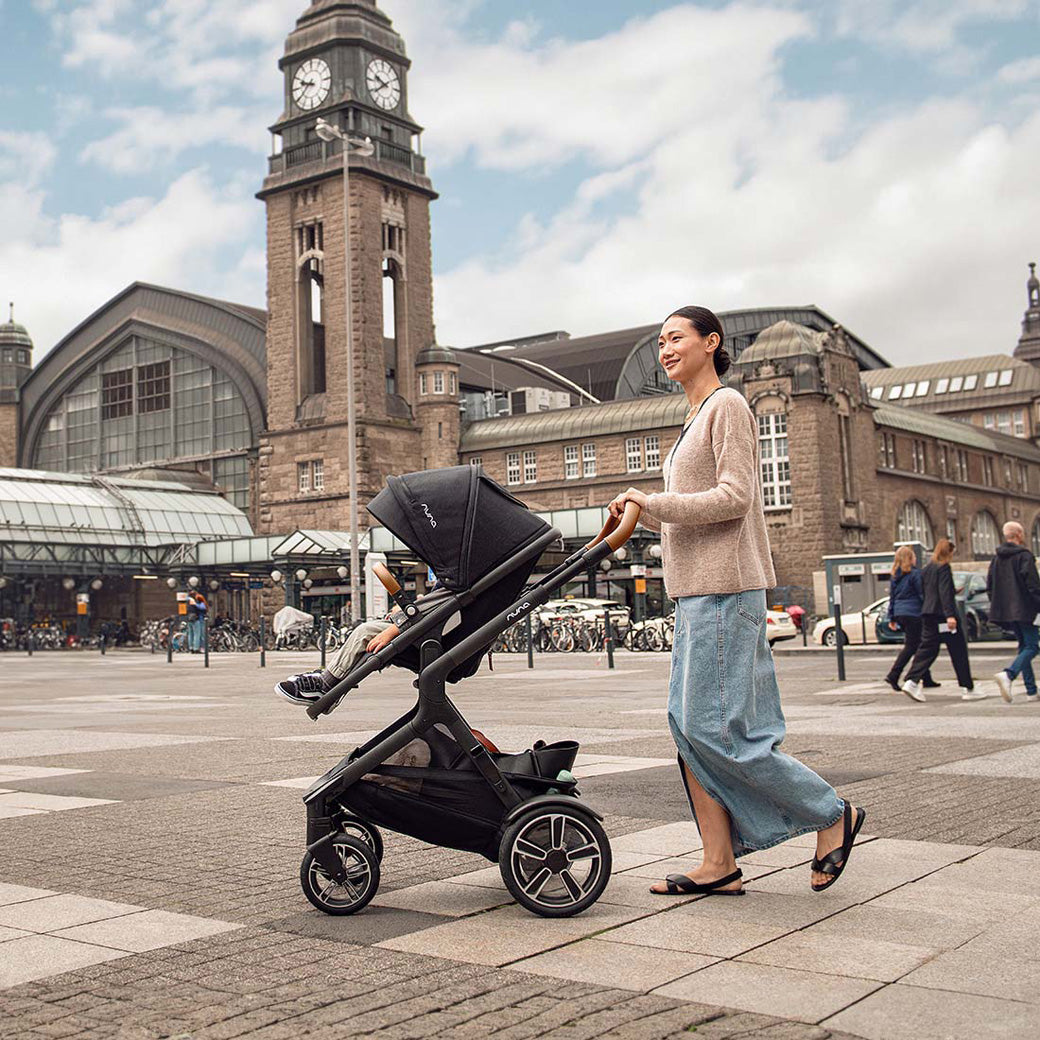 Mom on the street pushing her baby in the Nuna DEMI Next Stroller in -- Color_Caviar