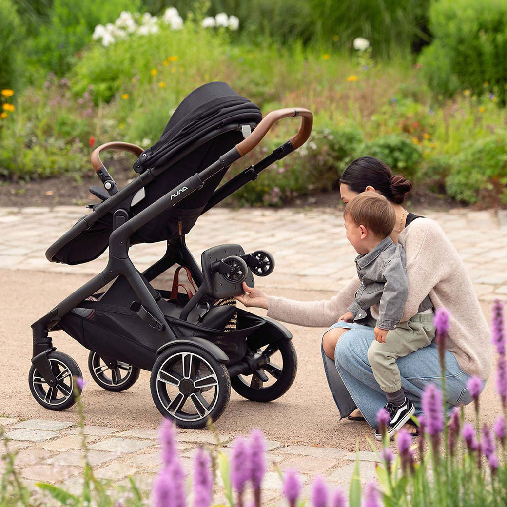 Mom showing a child the ride-along board of the Nuna DEMI Next Stroller in -- Color_Caviar