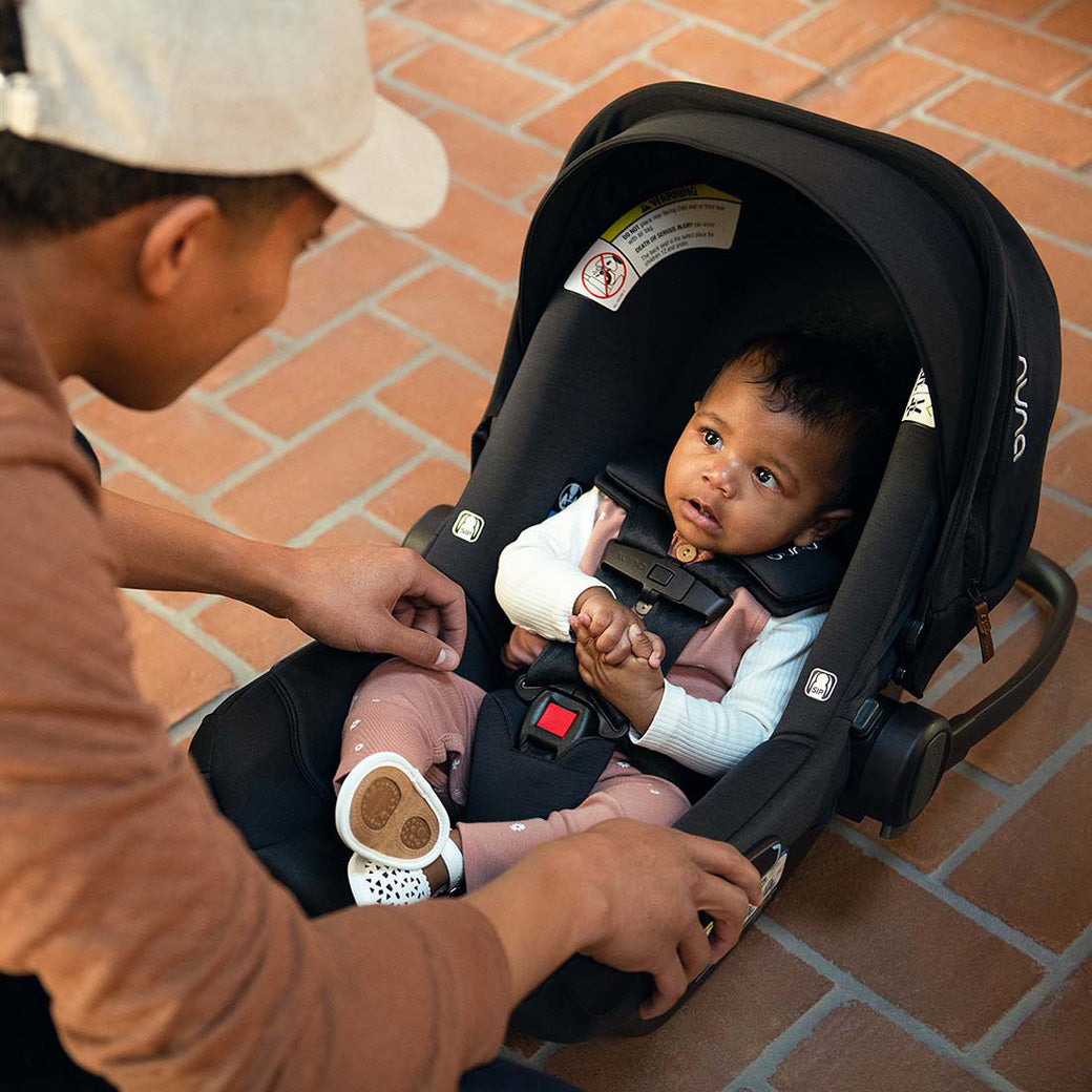 Dad looking at baby sitting in the Nuna PIPA Aire Infant Car Seat + PIPA Series Base in -- Color_Caviar