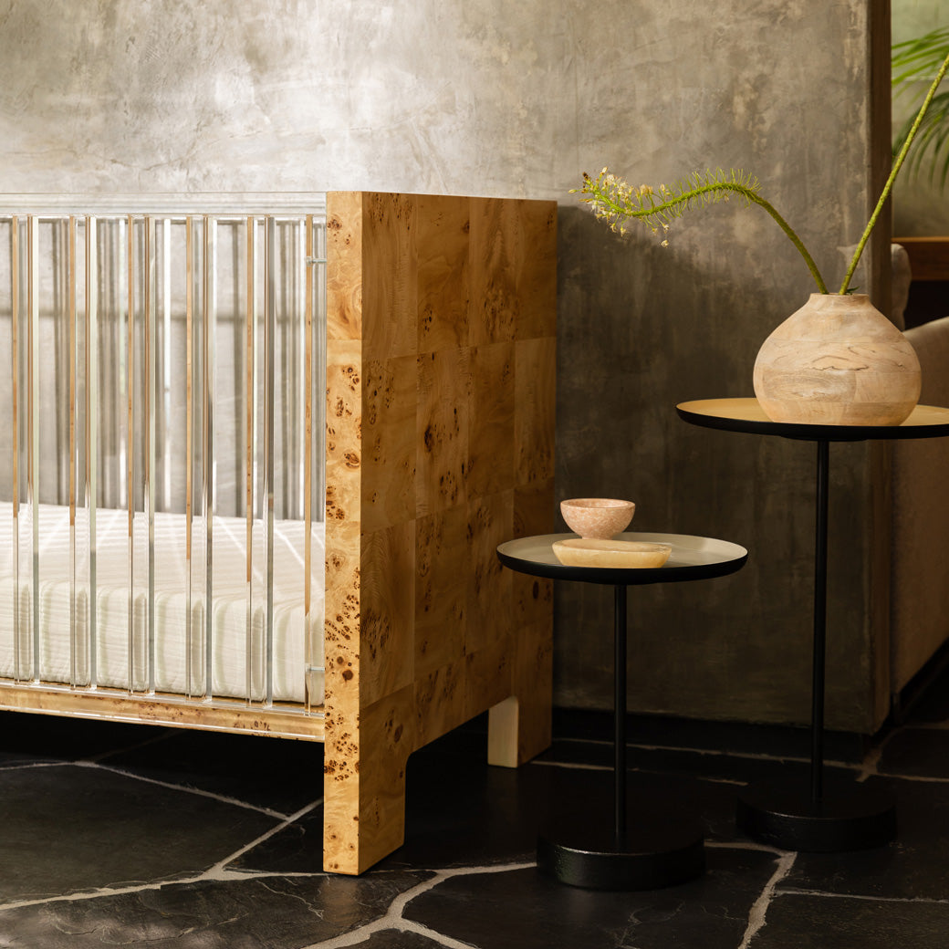 Closeup of Nursery Works Altair Crib next to a table in -- Color_Clear Acrylic with Burl