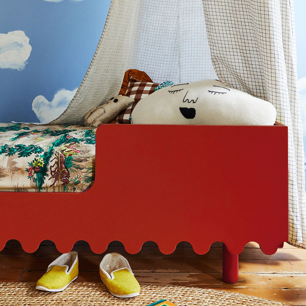Closeup of the side of Oeuf Moss Toddler Bed with pillows and toys  in -- Color_Tomato