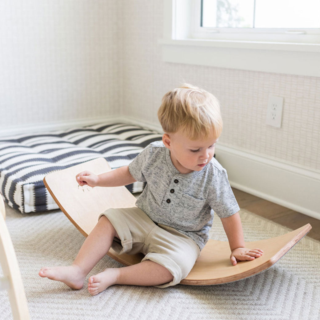 Child sitting on the Poppyseed Play Balance Board in -- Color_Gray Felt Bottom