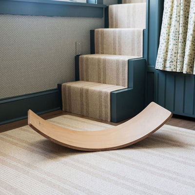 Poppyseed Play Balance Board next to stairs in -- Color_Natural Wood Bottom