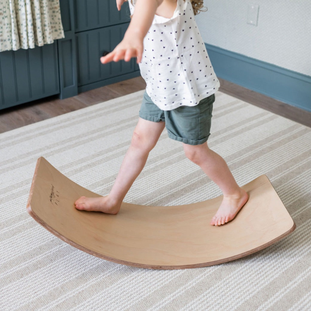 Child standing on the Poppyseed Play Balance Board in -- Color_Natural Wood Bottom