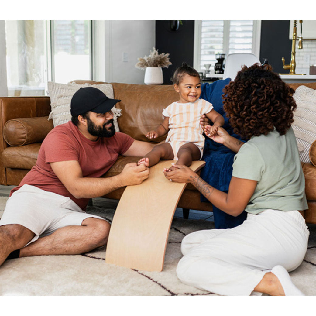 Mom and dad looking ad child on the Poppyseed Play Balance Board in -- Color_Natural Wood Bottom