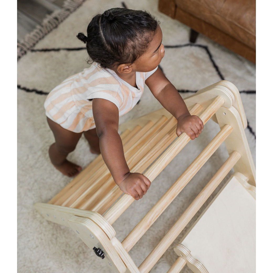 Baby standing and holding on to the Poppyseed Play Climbing Triangle & Ramp in -- Color_Natural