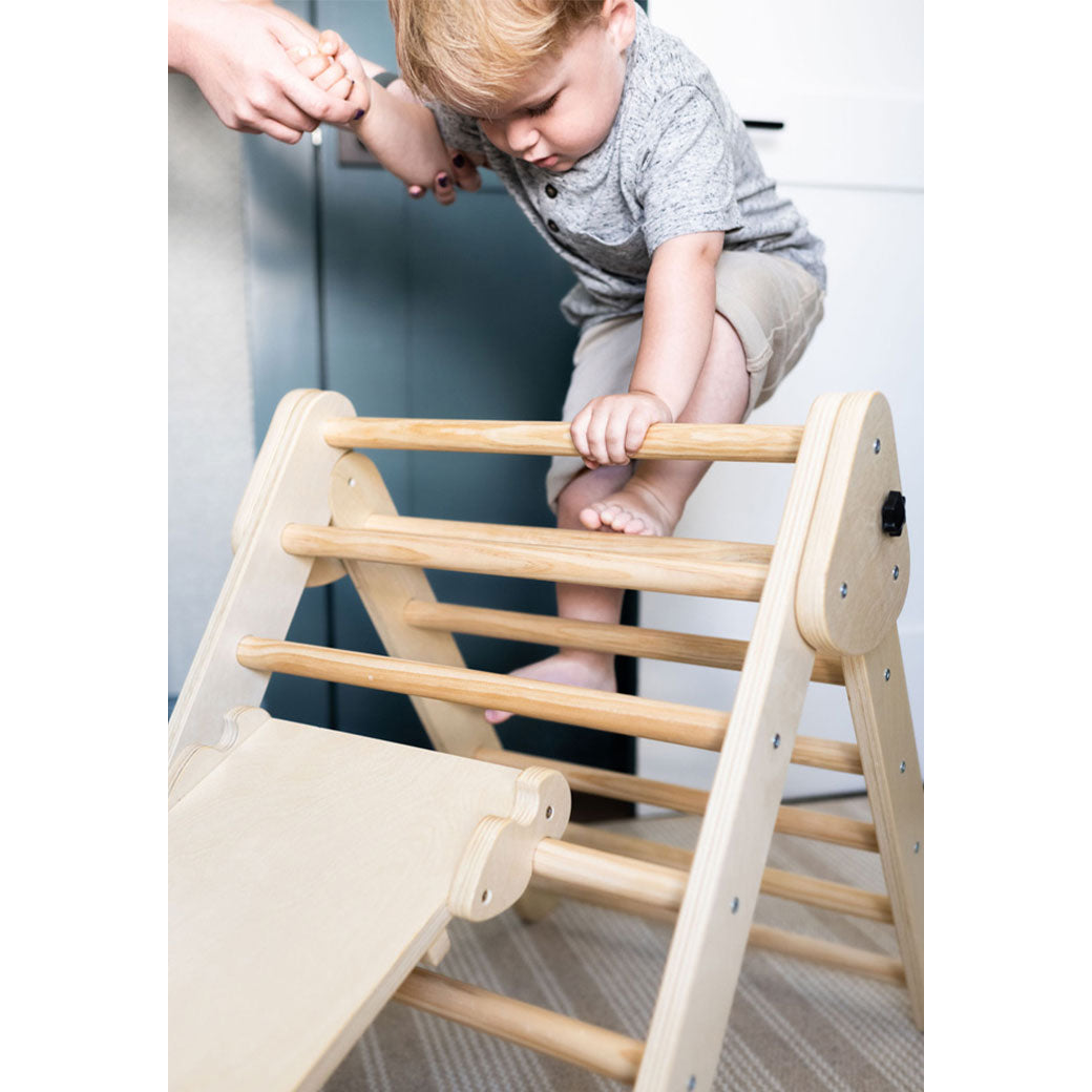 Child climbing on the Poppyseed Play Climbing Triangle & Ramp holding mom's hand in -- Color_Natural