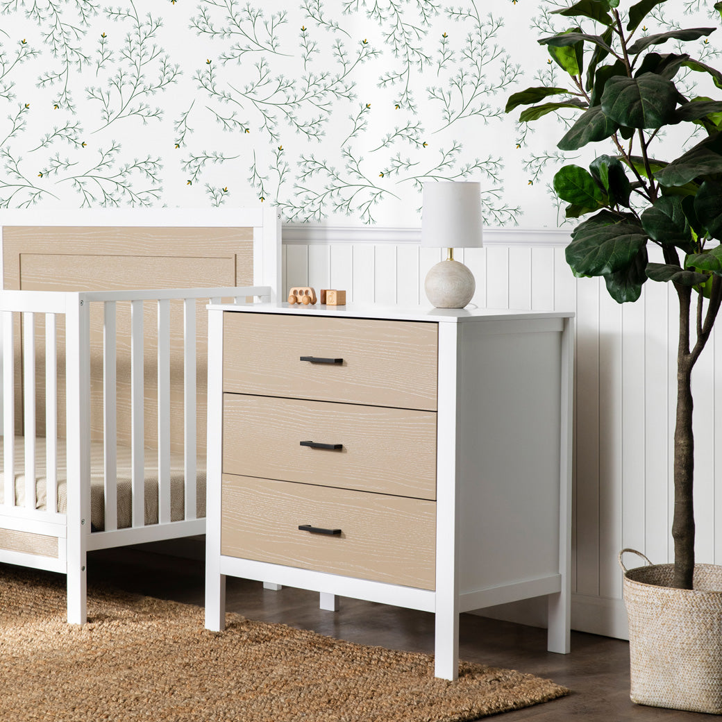 Carter's by DaVinci Radley 3-Drawer Dresser next to a crib and plant  in -- Color_White/Coastwood
