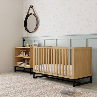 DaVinci's Ryder Convertible Cubby Changer & Bookcase next to a crib and under a mirror in -- Color_Honey