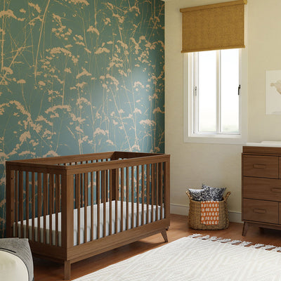 Babyletto's Scoot 3-in-1 Convertible Crib next to a basket and dresser  in -- Color_Natural Walnut
