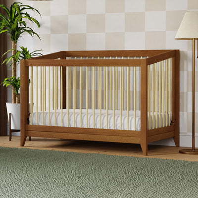 Babyletto's Sprout 4-in-1 Convertible Crib next to a plant in -- Color_Chestnut / Natural
