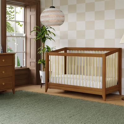 Babyletto's Sprout 4-in-1 Convertible Crib next to a plant and dresser in -- Color_Chestnut / Natural