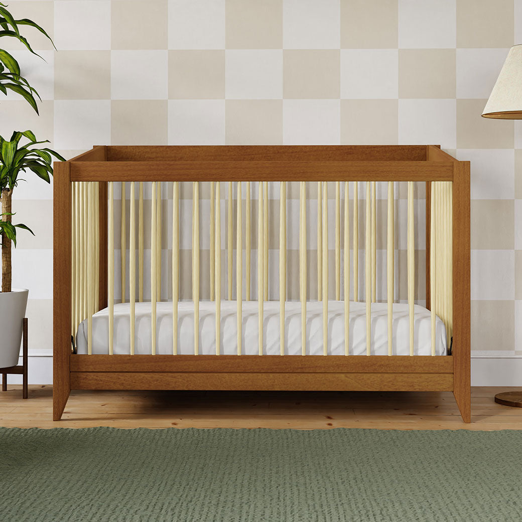 Front view of Babyletto's Sprout 4-in-1 Convertible Crib next to a plant in -- Color_Chestnut / Natural