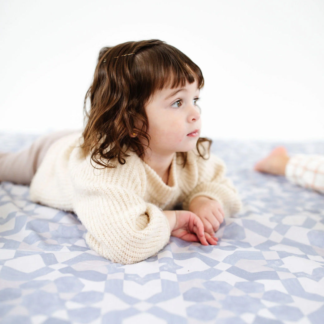 Toddler laying on the Toki Mats Padded Organic Cotton Play Mat in -- Color_Blue Tile