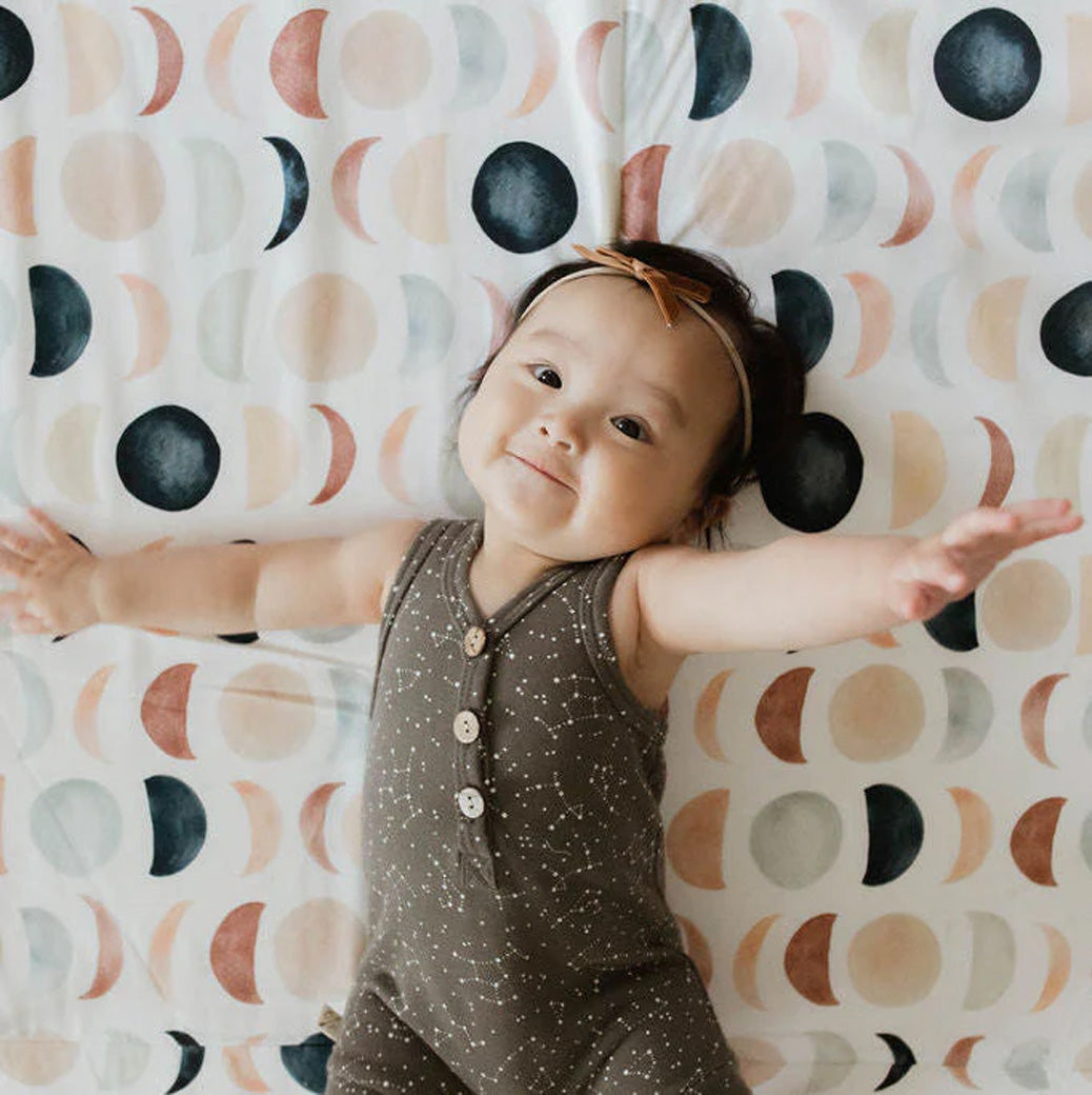 Baby smiling and laying on the Toki Mats Padded Organic Cotton Play Mat in -- Color_Lunar Phases