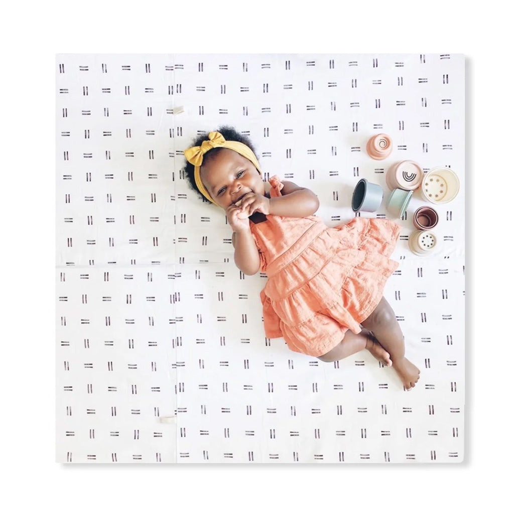Baby laying on the Toki Mats Padded Organic Cotton Play Mat with toys in -- Color_Mudcloth